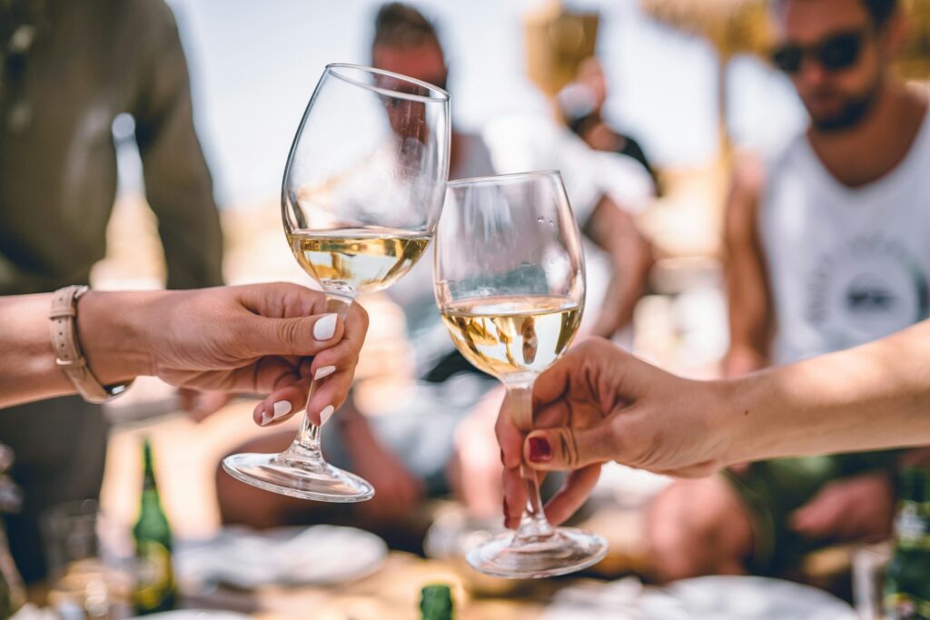 5 Tips For Choosing The Perfect Wine For Your Wedding Two people toasting with white wine outdoors.