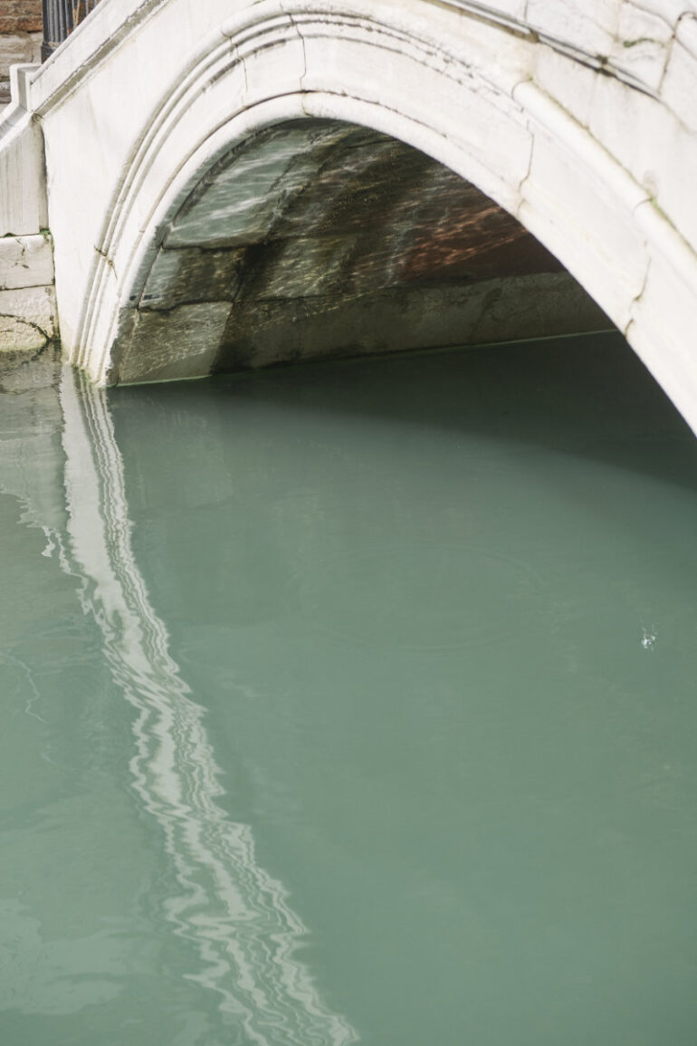 Reflection of stone bridge arch on water surface.