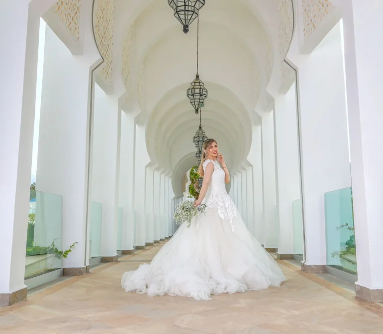 Bride posing in white dress in arched hallway.