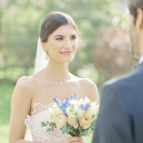 Bride holding bouquet, smiling at groom outdoor
