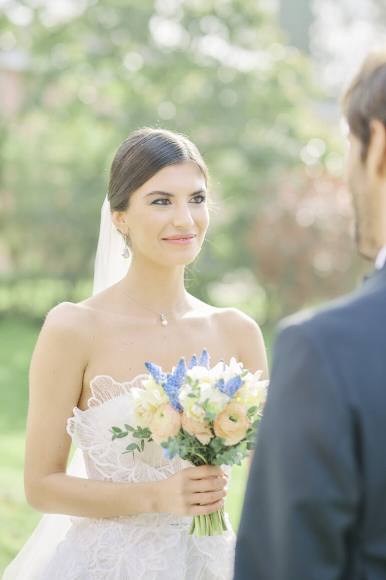 Bride holding bouquet, smiling at groom outdoor