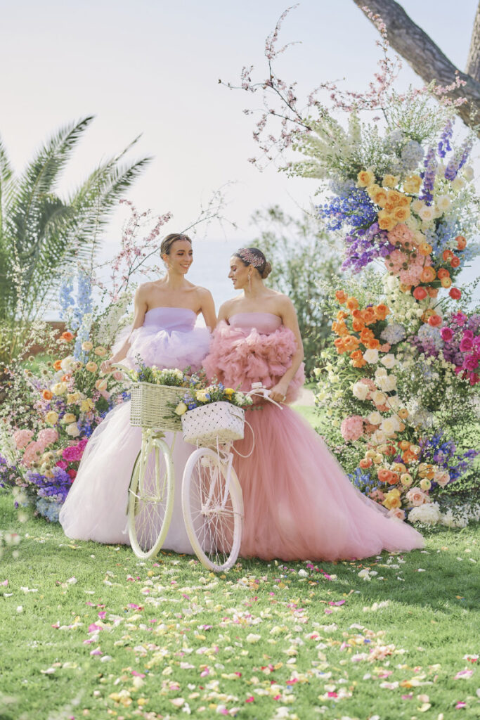 A Vision Of Venice Weddings Two women in gowns beside flower-adorned bicycle.