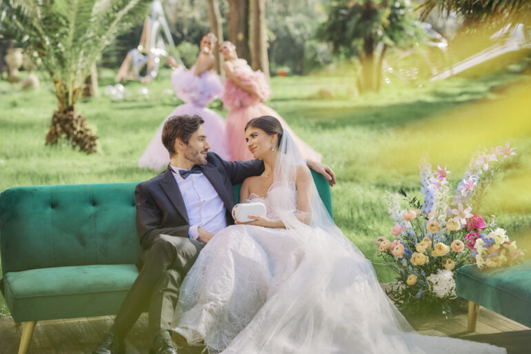 Bride and groom sitting on green sofa outdoors.