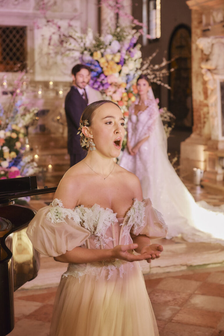 Opera singer performing at wedding ceremony, bride and groom behind.
