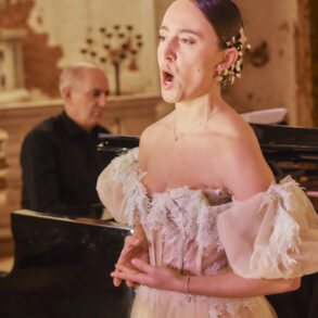 Woman singing with pianist in the background.