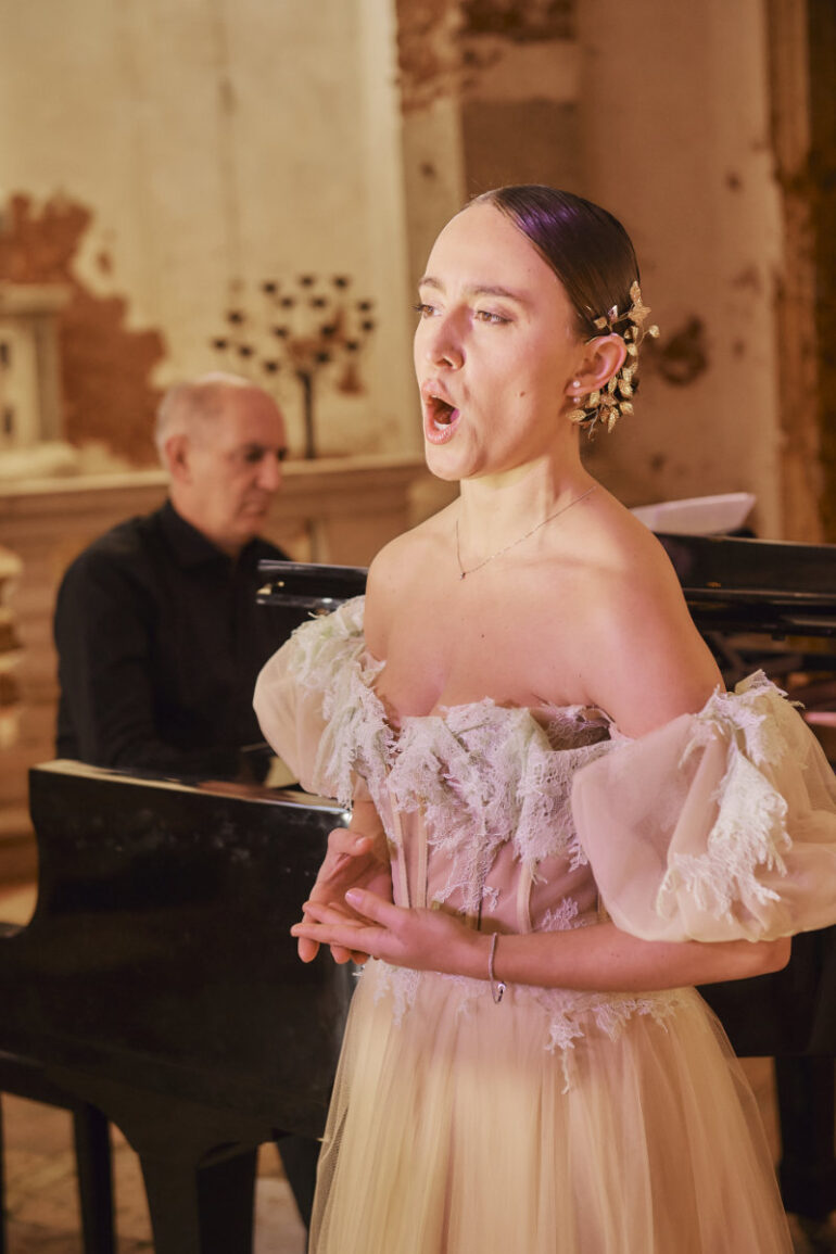 Woman singing with pianist in the background.