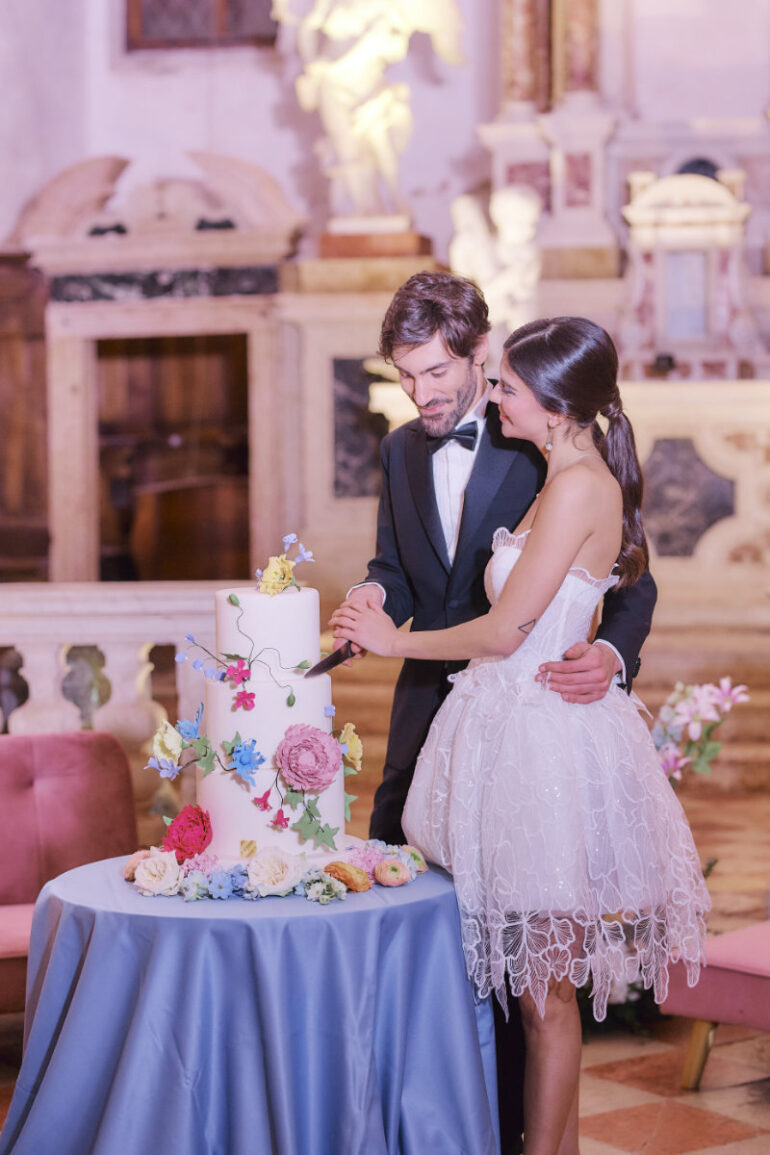 Couple cutting floral wedding cake in elegant venue.