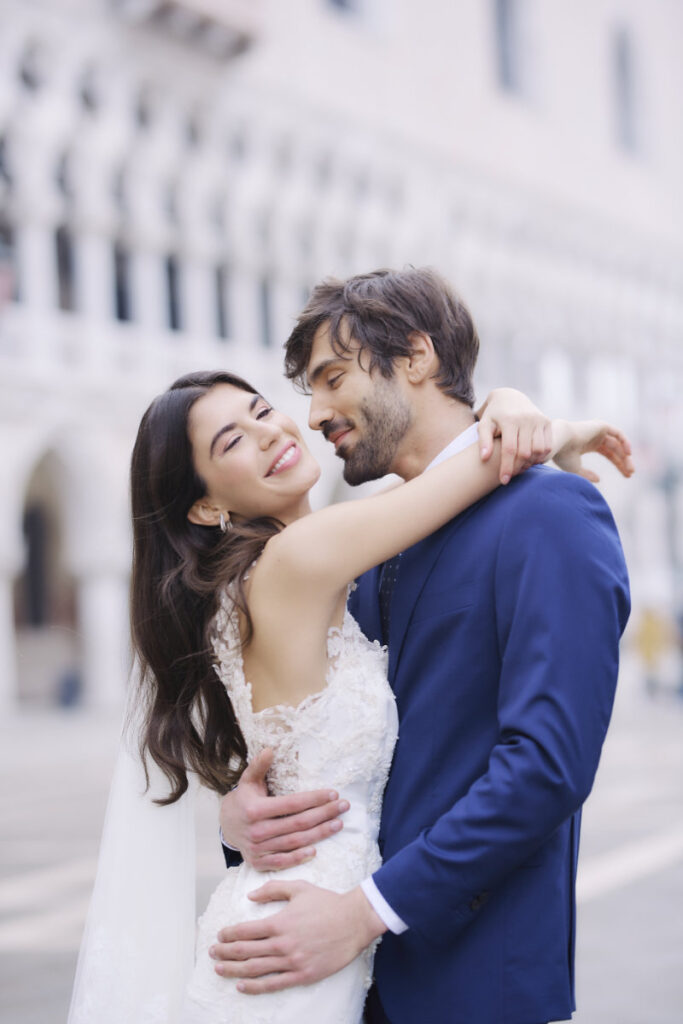 A Vision Of Venice Weddings Wedding couple embracing, smiling outside historical building.