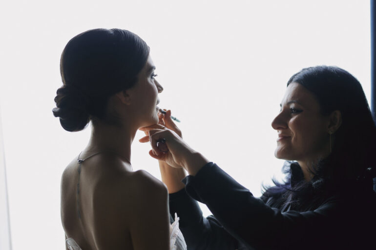 Makeup artist applying lipstick to bride.