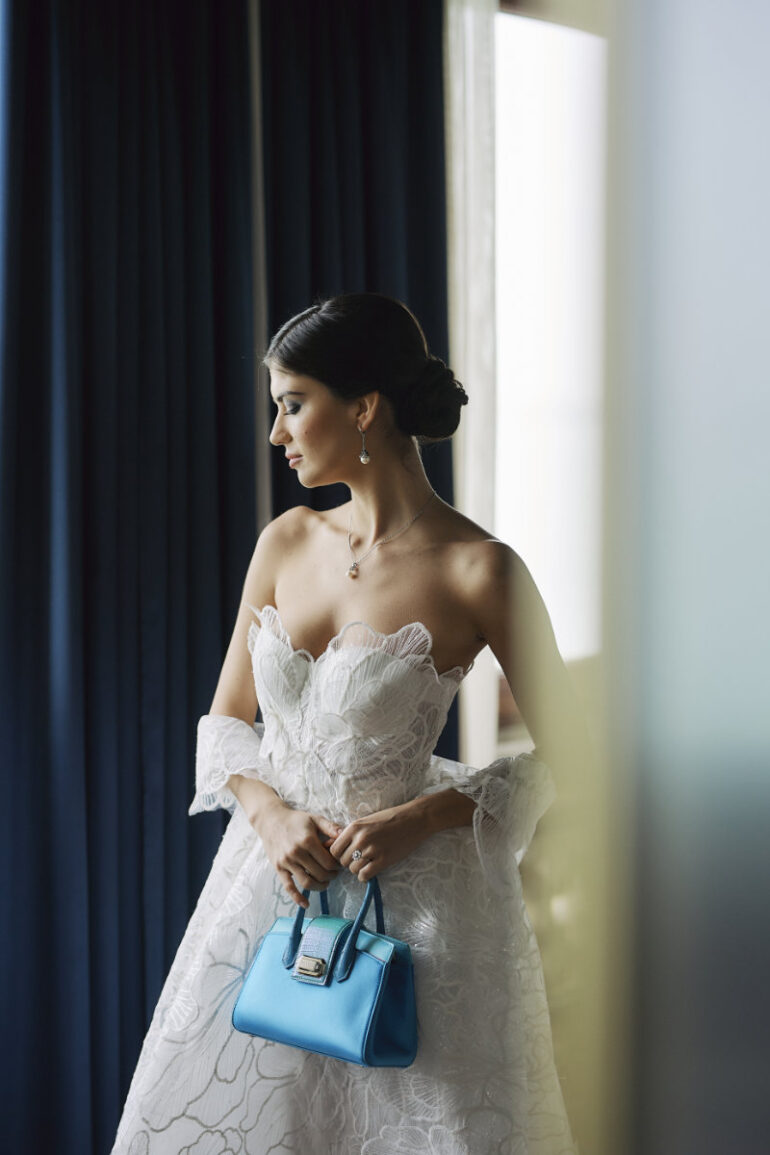 Bride holding blue handbag in white wedding dress.