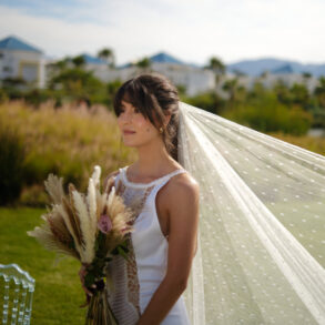 Bride in white dress holding bouquet outdoors.