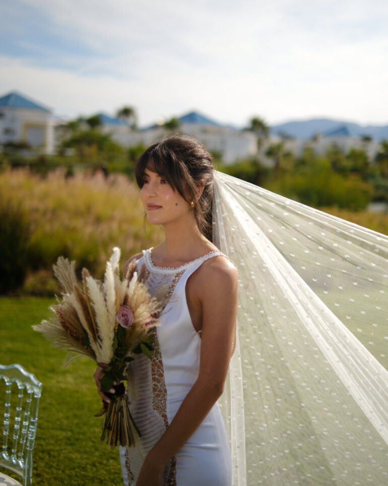 Bride in white dress holding bouquet outdoors.