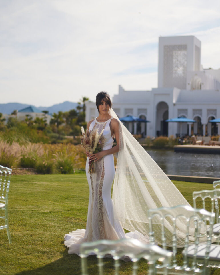 Bride in white dress with long veil outside.
