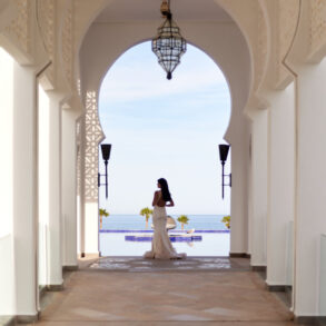 Woman in white dress standing in archway, ocean view