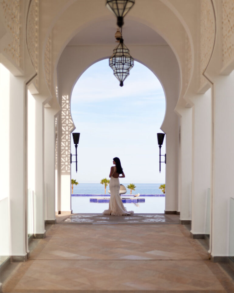Woman in white dress standing in archway, ocean view