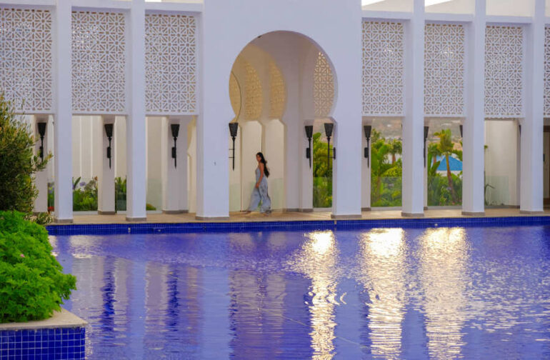Woman walking by building with pool reflections.