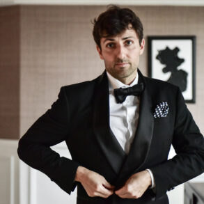 Man in tuxedo adjusting jacket indoors.