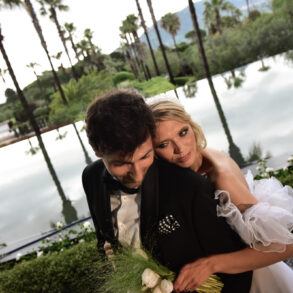 Bride and groom embrace by a reflective pond.