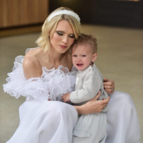 Woman in white holding crying toddler indoors.