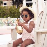 Child sipping drink in pineapple cup, summer hat on.