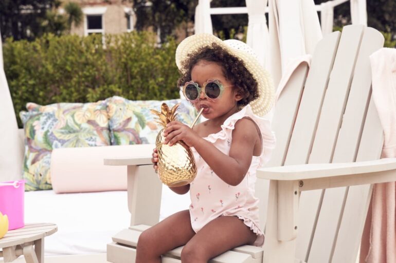 Child sipping drink in pineapple cup, summer hat on.