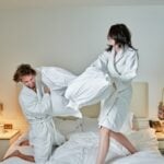 Couple playfully having a pillow fight in robes.