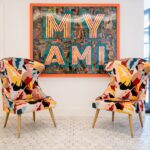 Colourful chairs and 'MY AMI' wall art in room.