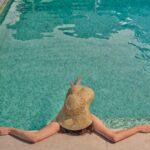 Person relaxing by the pool in sun hat.