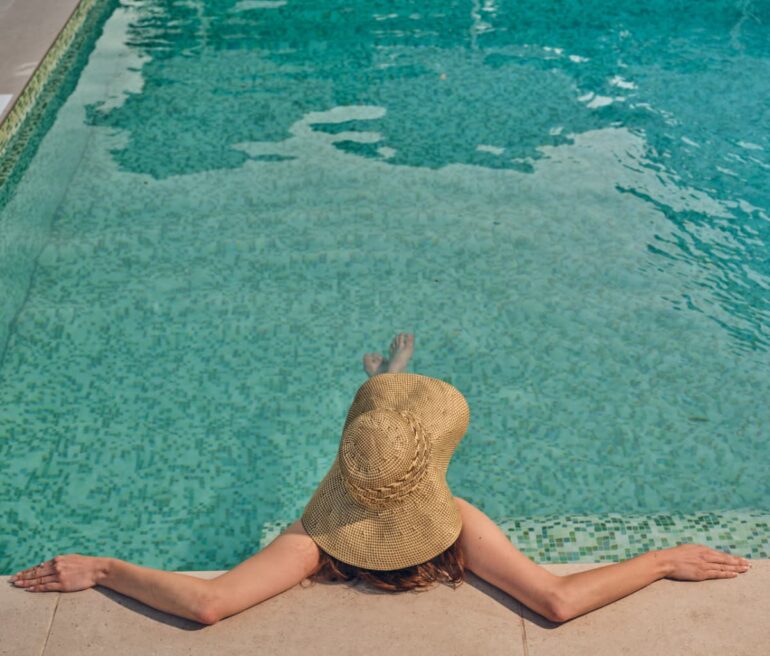 Person relaxing by the pool in sun hat.