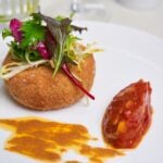 Gourmet dish with croquette, salad, and sauce.