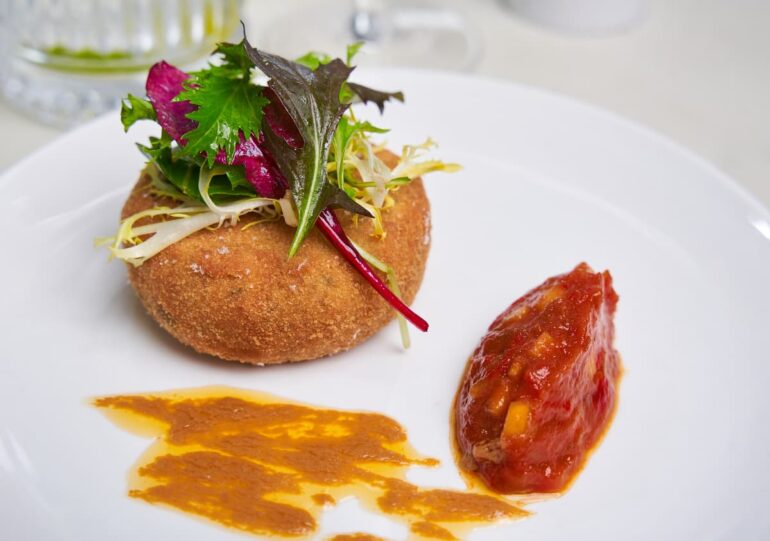 Gourmet dish with croquette, salad, and sauce.