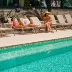 Three people sunbathing by a swimming pool.