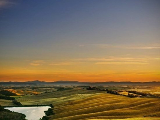 A beautiful sunset over rolling hills and a tranquil water body.