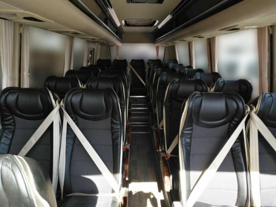 Empty bus interior featuring rows of seats with safety belts.