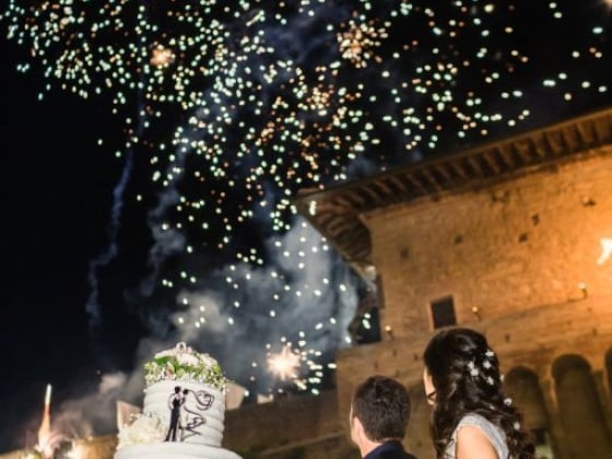 A couple admires fireworks above their wedding cake.