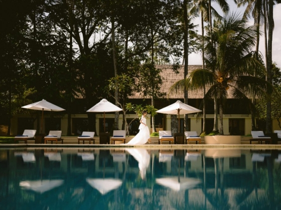 A serene scene of a bride near a pool surrounded by palm trees.