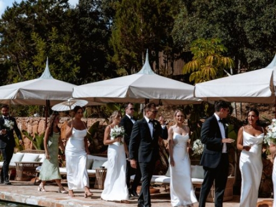 A bridal party strolls by the pool, dressed in white gowns and suits.