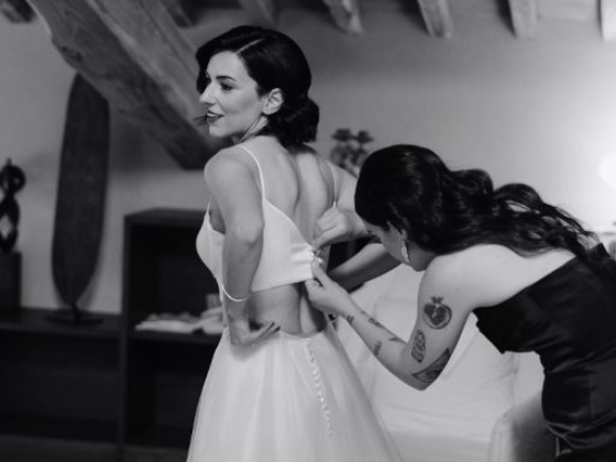 A bride receives help fastening her wedding dress.