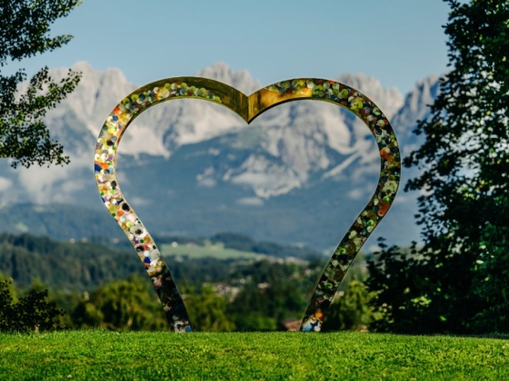 A colorful heart sculpture amidst scenic mountains.