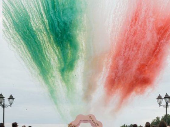 A couple sharing a kiss as colorful smoke explodes above them.