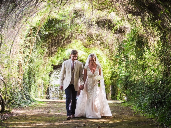 A couple strolls hand in hand in a garden setting.
