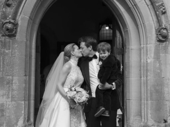 A happy couple shares a kiss with their child in a doorway.