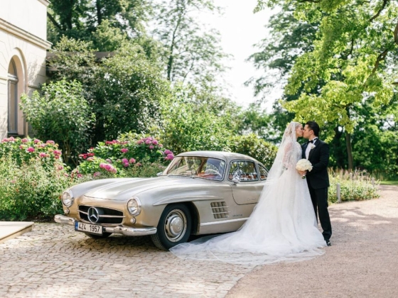 A romantic moment beside a classic car in a beautiful setting.