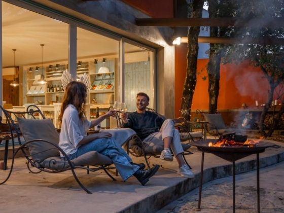 Two friends relax and toast by a fire at night.