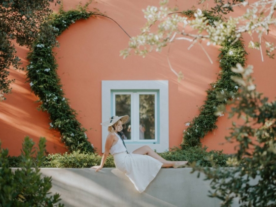 A stylish woman poses by a heart-shaped vine against a vibrant backdrop.