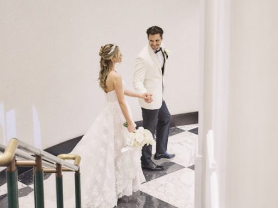 A couple descends a marble staircase, holding hands.