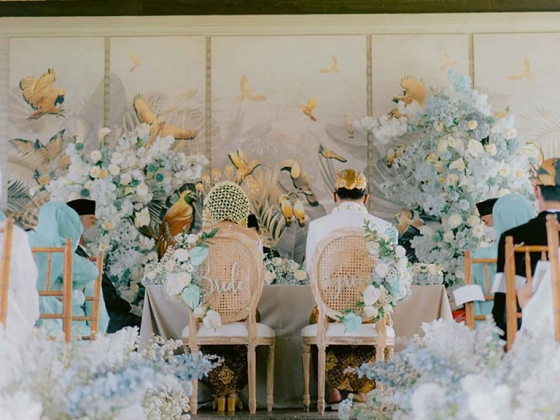 Couple seated, adorned with flowers in a serene setting.