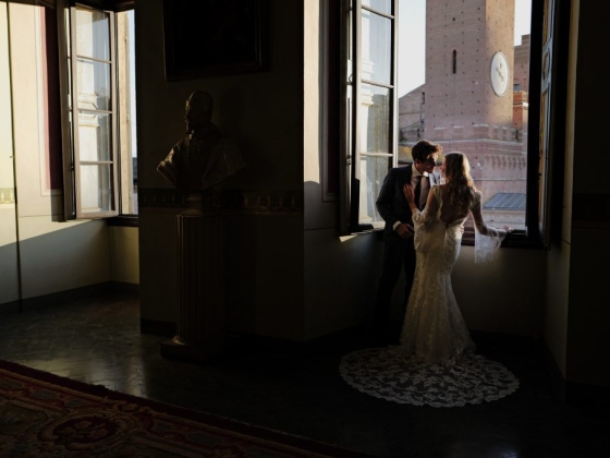 A bride and groom share a kiss in a sunlit room.
