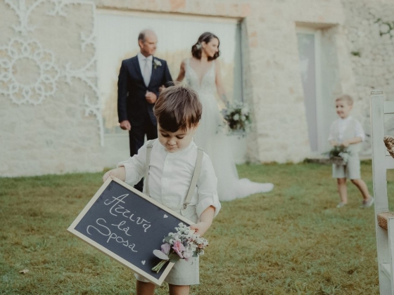 A boy with a sign in a wedding setting, bride and groom in background.