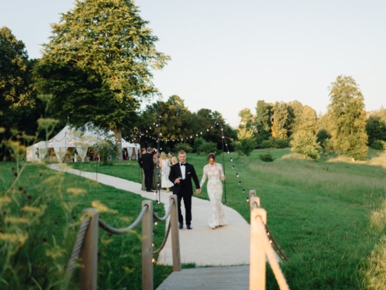 A couple strolls on a path toward a wedding celebration.